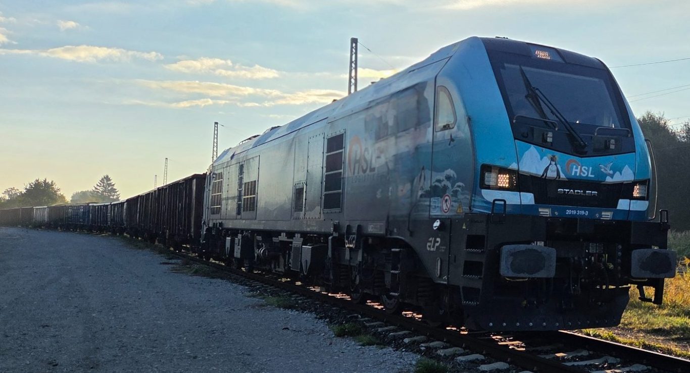 Euro 9000 bei der Rübenverladung Moderne Lokomotive fährt auf Schienen, umgeben von mehreren Güterwagen im Morgenlicht.